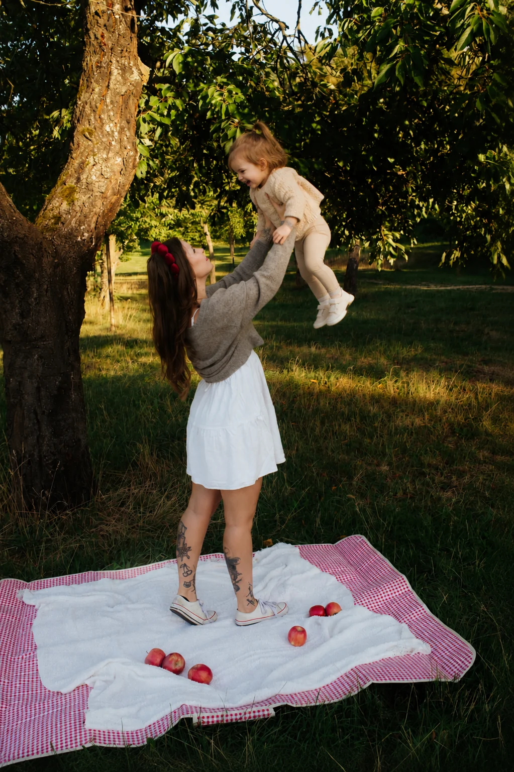 Žena zvedá malé dítě na piknikové dece pod stromem